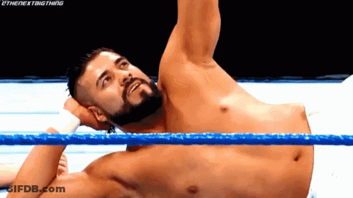 A Man With A Beard Is Laying In A Wrestling Ring With His Arm Up . GIF