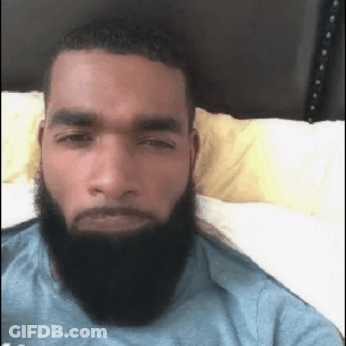 A Man With A Beard Is Laying In Bed And Looking At The Camera . GIF