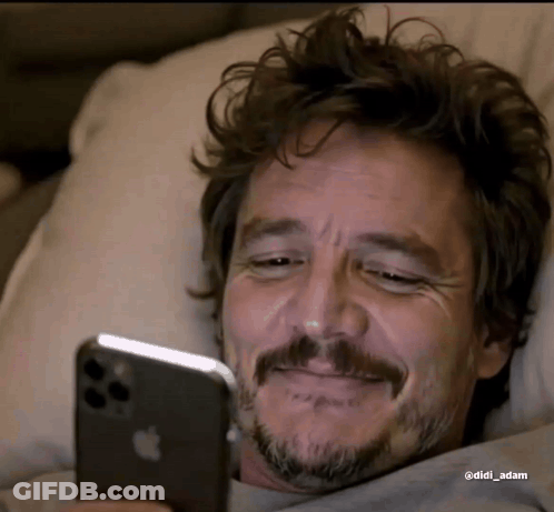 A Man With A Beard Is Laying In Bed Looking At His Iphone . GIF