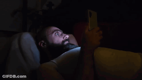 A Man With A Beard Is Laying In Bed Using A Cell Phone GIF