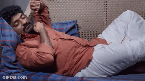 A Man With A Beard Is Laying On A Bed With His Legs Crossed GIF