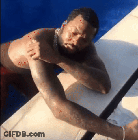 A Man With A Beard Is Laying On A Ledge In A Pool GIF