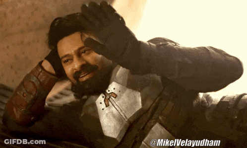 A Man With A Beard Is Laying On The Floor With The Hashtag @Mikelvelayudham On The Bottom Right GIF