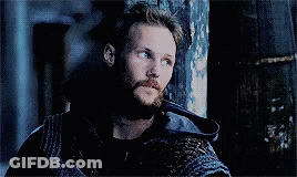 A Man With A Beard Is Leaning Against A Wooden Wall In A Dark Room . GIF