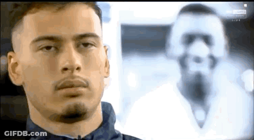 A Man With A Beard Is Looking At A Picture Of A Man With A Beard . GIF