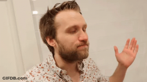 A Man With A Beard Is Looking At Himself In A Bathroom Mirror . GIF
