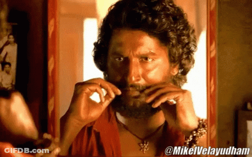 A Man With A Beard Is Looking At Himself In A Mirror With @Mikelvelayudham Written On The Bottom GIF