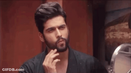 A Man With A Beard Is Looking At Himself In The Mirror GIF