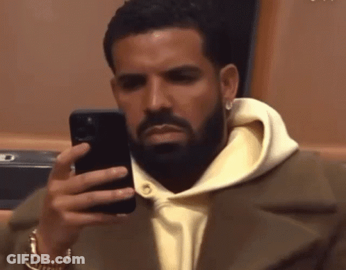 A Man With A Beard Is Looking At His Cell Phone GIF