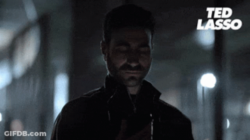 A Man With A Beard Is Looking At His Phone With Ted Lasso Written On The Bottom GIF