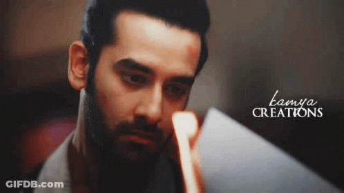 A Man With A Beard Is Looking At Something In A Mirror . GIF