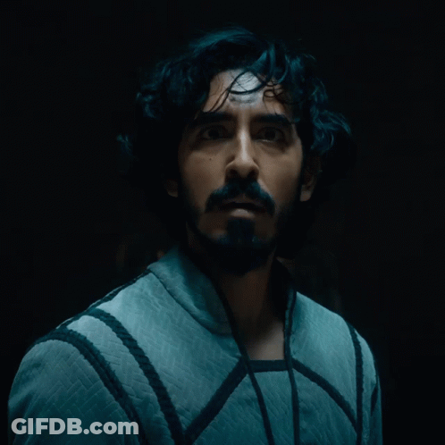 A Man With A Beard Is Looking At The Camera In A Dark Room GIF