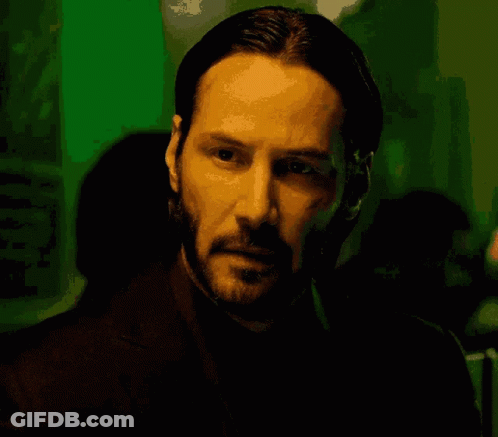 A Man With A Beard Is Looking At The Camera In A Dark Room GIF