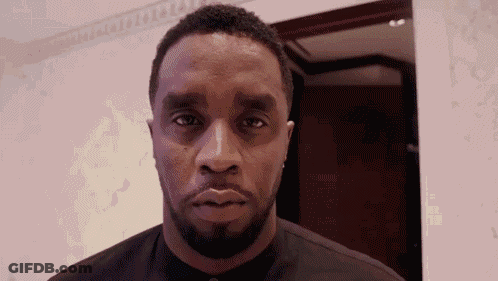 A Man With A Beard Is Looking At The Camera While Wearing A Black Shirt . GIF