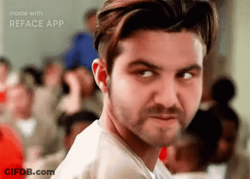 A Man With A Beard Is Looking At The Camera With A Crowd Of People In The Background . GIF