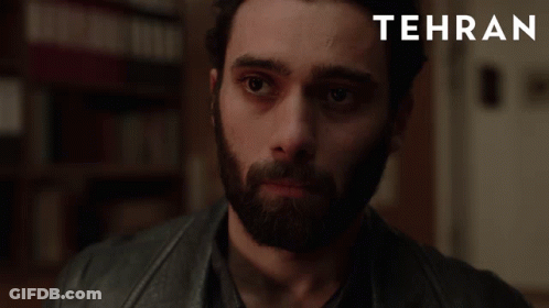 A Man With A Beard Is Looking At The Camera With Tehran Written In The Corner GIF