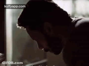 A Man With A Beard Is Looking Down At Something . GIF