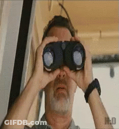 A Man With A Beard Is Looking Through Binoculars With The Letter H On The Bottom Left GIF