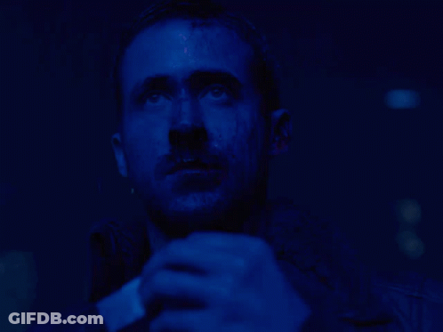 A Man With A Beard Is Looking Up In A Dark Blue Room GIF
