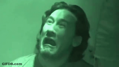 A Man With A Beard Is Making A Funny Face In A Dark Room . GIF