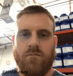 A Man With A Beard Is Making A Funny Face In Front Of A Shelf Of Chemicals . GIF