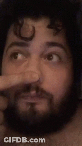 A Man With A Beard Is Making A Funny Face While Holding His Nose . GIF