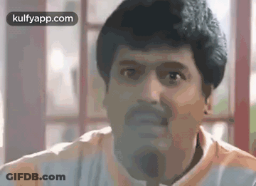 A Man With A Beard Is Making A Funny Face While Sitting In Front Of A Window . GIF
