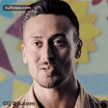 A Man With A Beard Is Making A Funny Face While Standing In Front Of A Colorful Background . GIF