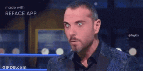 A Man With A Beard Is Making A Funny Face While Wearing A Blue Jacket And Black Shirt . GIF