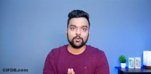A Man With A Beard Is Making A Funny Face With His Hands Outstretched In Front Of A Blue Wall . GIF