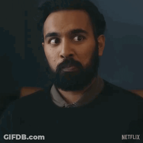 A Man With A Beard Is Making A Surprised Face In A Dark Room . GIF
