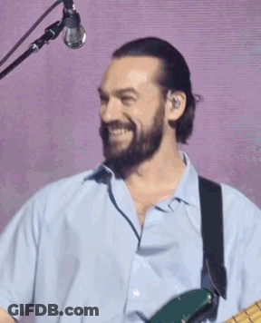 A Man With A Beard Is Playing A Guitar In Front Of A Microphone And Smiling . GIF