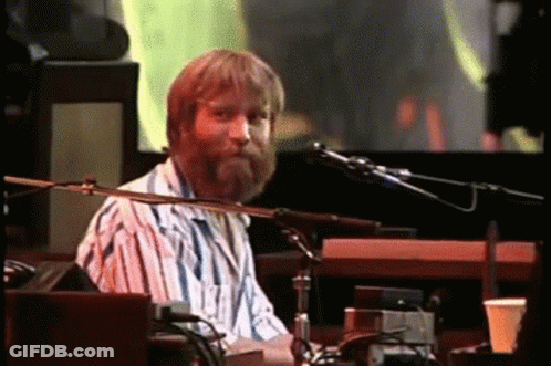 A Man With A Beard Is Playing A Keyboard And Singing Into A Microphone On A Stage . GIF