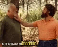 A Man With A Beard Is Putting His Hand On Another Man 'S Face While Another Man Says Shhhh . GIF