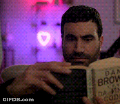A Man With A Beard Is Reading A Book Called Dan Brown 'S Damn Code GIF
