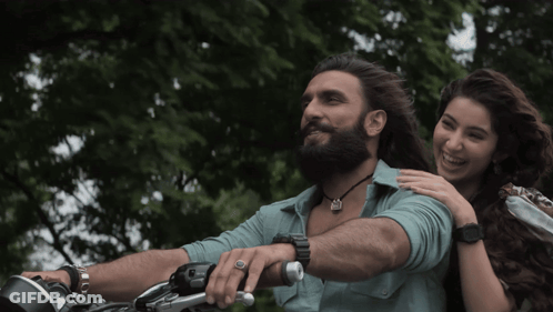 A Man With A Beard Is Riding A Motorcycle While A Woman Holds His Arm GIF