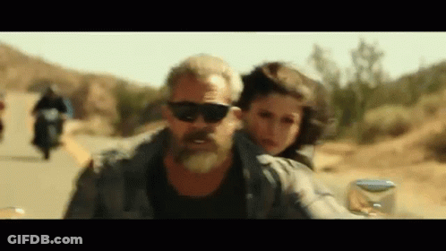 A Man With A Beard Is Riding A Motorcycle With A Woman On The Back . GIF