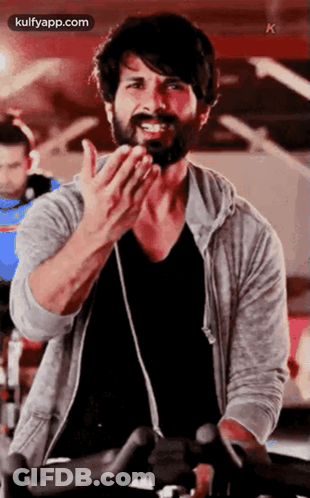 A Man With A Beard Is Riding An Exercise Bike In A Gym And Clapping . GIF