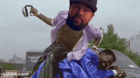 A Man With A Beard Is Riding Another Man On His Shoulders . GIF