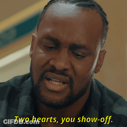 A Man With A Beard Is Saying Two Hearts You Show Off GIF