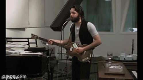 A Man With A Beard Is Singing Into A Microphone While Playing A Guitar . GIF