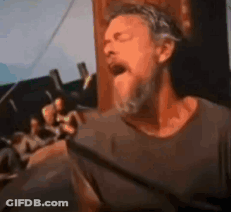 A Man With A Beard Is Singing Into A Microphone While Standing In Front Of A Crowd . GIF