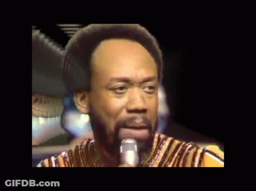 A Man With A Beard Is Singing Into A Microphone While Wearing A Striped Shirt GIF