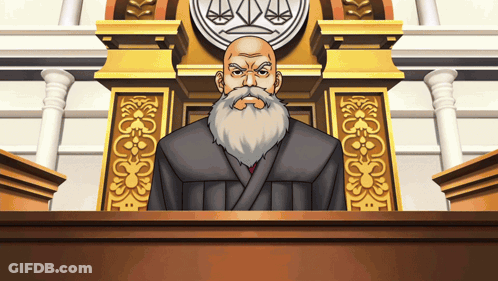 A Man With A Beard Is Sitting At A Podium In Front Of A Justice Symbol GIF