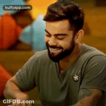 A Man With A Beard Is Sitting At A Table And Smiling . GIF