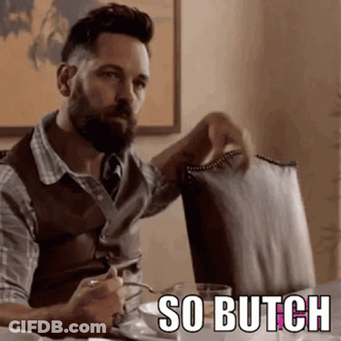 A Man With A Beard Is Sitting At A Table Holding A Chair And A Cup Of Coffee . GIF