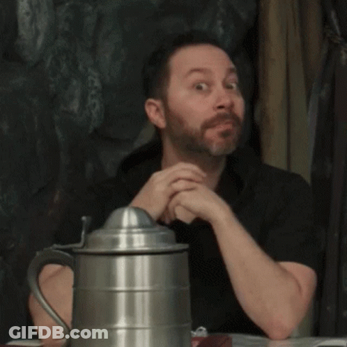 A Man With A Beard Is Sitting At A Table Next To A Metal Pitcher GIF