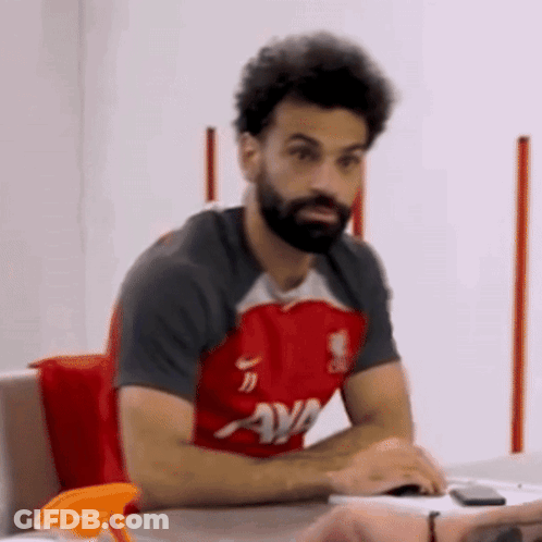 A Man With A Beard Is Sitting At A Table Wearing A Red Shirt That Says Ava On It GIF