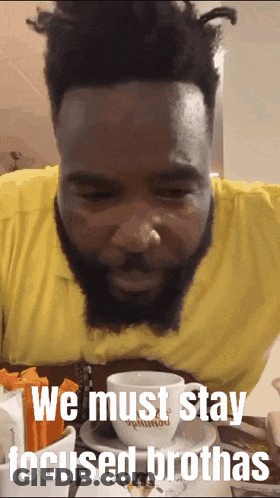 A Man With A Beard Is Sitting At A Table With A Cup Of Coffee And The Words We Must Stay Focused Brothas GIF
