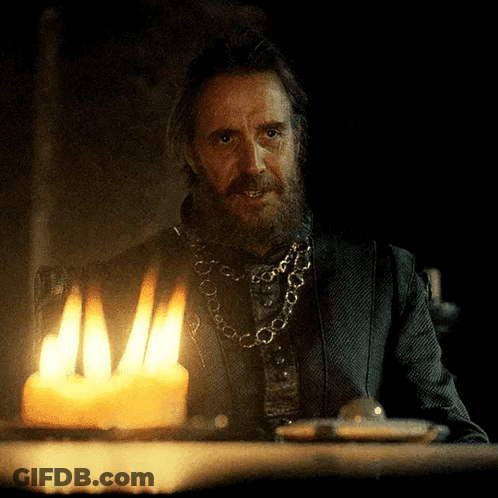 A Man With A Beard Is Sitting At A Table With A Lit Candle In Front Of Him GIF
